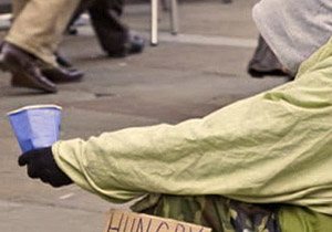 A homeless person holds out a cup to people passing by