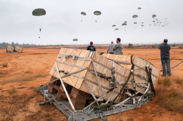 Container Unitized Bulk Equipment, or CUBE, crates rest in the foreground after a test airdrop Nov. 10, 2011, at Camp MacKall, N.C. The CUBE system will deliver water and fuel to remote forward operating bases.