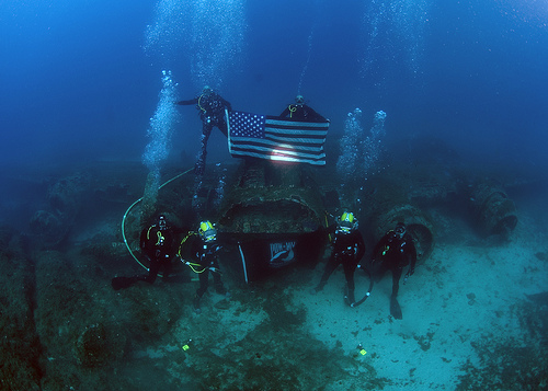 <p>From top left, U.S. Navy Chief Explosive Ordnance Disposal Technician Matthew Harrison, Chief Navy Diver Eric Eberle, Navy Diver 3rd Class Brian Stewart, Senior Chief Master Diver Michael Woods, Navy Diver 2nd Class Sean Mcconnell and Chief Warrant Officer John Sullivan, all assigned to Mobile Diving and Salvage Unit 2, Company 4 and the Joint Prisoner of War/Missing In Action (POW/MIA) Accounting Command (JPAC), hold an American flag and a POW/MIA flag Oct. 19, 2012, in Calvi, France, at the site of the wreckage of a B-17 Flying Fortress aircraft that was shot down and sunk during World War II. The team was deployed alongside JPAC aboard salvage ship USNS Grapple (T-ARS-53) as part of a 30-day underwater recovery mission for an unaccounted-for U.S. Service member who went missing during the crash. JPAC conducts global search, recovery and laboratory operations to identify unaccounted-for Americans from past conflicts. (DoD photo by Mass Communication Specialist 2nd Class Martin Carey, U.S. Navy/Released)</p>