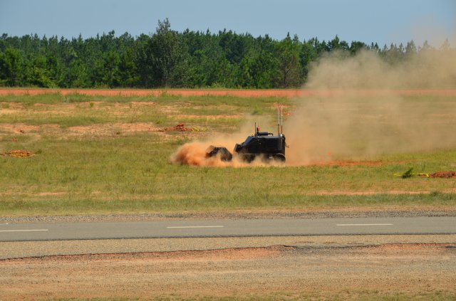 A specially designed, unmanned improvised explosive device defeat vehicle traverses the Robotics Rodeo course. An arm aboard the vehicle lowers over a simulated threat site and blades begin digging to disarm the device. The 2012 Robotics Rodeo held at Fort Benning, Ga., June 20-29, 2012, allowed manufacturers to showcase the latest robotics technology designed to defeat battlefield threats, especially improvised explosive devices.