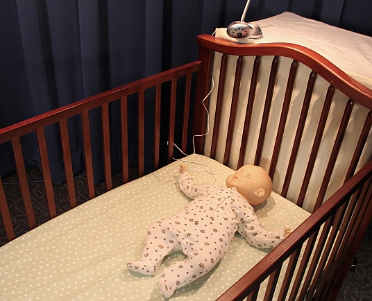 Baby in a crib with a video monitor cord next to the crib