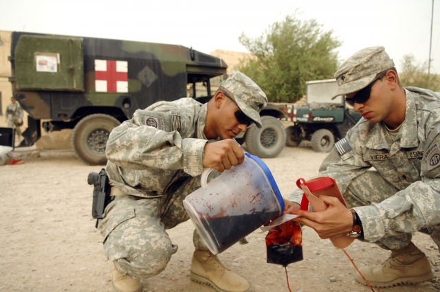 Sgt. Joel Ruiz and Spc. Osniel Viera, from the 82nd Sustainment Brigade, pour fake blood into an intravenous bag during a combat casualty treatment course for Iraqi police recruits at Camp Mitica.