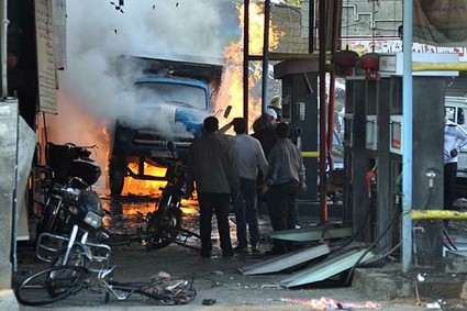 In this photo released by the Syrian official news agency SANA, Syrian citizens stand near a burning truck that was destroyed by two cars bombs, at Jaramana neighborhood, in the suburb of Damascus, Syria, Wednesday, Nov. 28, 2012. 