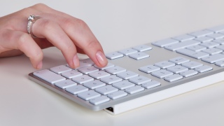 Eine Frauenhand tippt auf flacher Computertastatur