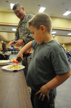 Jason Ray Williams, 6, pours syrup on his pancakes at the Fat Tuesday Pancake Supper, Feb. 21, as Chap. (Col.) James Watson, senior installation chaplain, looks on.
