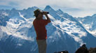 man looking through binoculars at a mountain range 