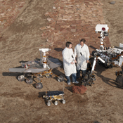 Two spacecraft engineers stand with three generations of Mars rovers developed at NASA's JPL, Pasadena, Ca. Front and center is a flight spare of Sojourner, left is a working sibling to Spirit and Opportunity, right is test rover Curiosity.