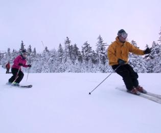 Man and woman skiing together down mountain.