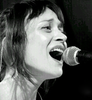 A black and white headshot of Fiona Apple singing into a microphone