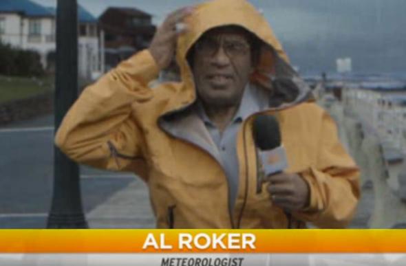 Weatherman Al Roker dressed in foul-weather gear with microphone, standing in a driving rain on the waterfront.