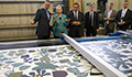 People viewing a  printed fabric in a factory. (Photo Credit: State Department)