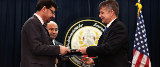 two men in front of flag and seal