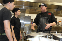 Chef Mark Millwood, right, owner of a local restaurant and former food service specialist for the U. S. Navy, explains how to properly coat catfish in season to Cpl. Vidal Rios, left, Cpl. Andrea Hillebrand, center, two food service specialist with Combat Logistics Regiment-17, at the Las Pulgas Mess hall here Feb. 6. Millwood shared his knowledge he gained from his 26 years of cooking experience with the Marines.