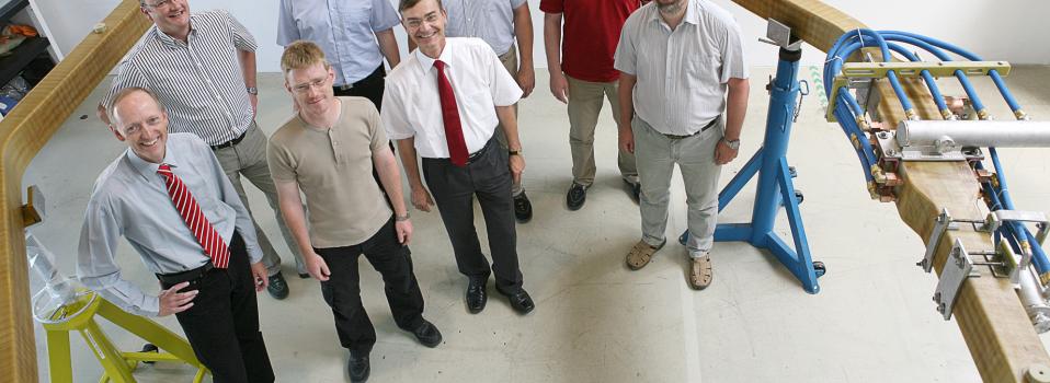 Max Planck staffers with delivered trim coil. Front row from left: Dr. Thomas Rummel, head of magnet and cryostat subdivision; Stefan Freundt, engineer; Dr. Hans-Stephan Bosch, associate director for coordination; Victor Bykov, engineer. Back row, from left: Konrad Risse, trim coil project leader; Frank Füllenbach, engineer; Mathias Gottschewsky, project control engineer; Matthias Köppen, engineer.