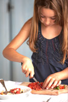 A girl chopping vegetables for a meal.