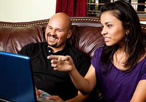 Laughing couple on sofa with laptop computer. She is pointing at something funny