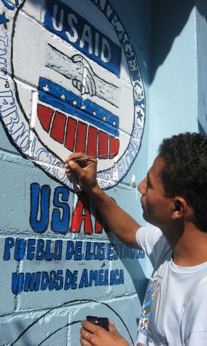 A young man paints the USAID logo on the wall of an outreach center