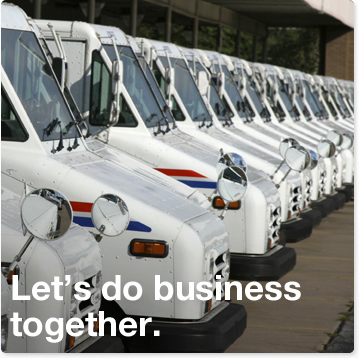 Let's do business together. A fleet of USPS delivery trucks lined uniformly in a horizontal row. The trucks are parked outside a Post Office in a parking lot.
