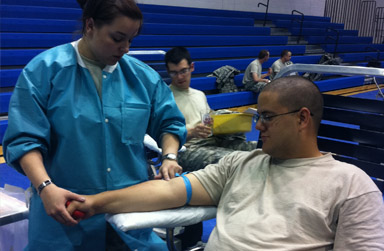 Spc. Aaron Kamiaz, assigned to Raymond W. Bliss Army Health Center at Fort Huachuca, Ariz., watches as phlebotomist Staff Sgt. Angela Gehers applies the tourniquet to Kamiaz s arm in preparation to donate blood.  As a medic, Kamiaz has seen the need for blood and is giving back during the monthly blood drive at Fort Huachuca.