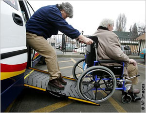 A bus driver pulls a man in a wheelchair up an access ramp.