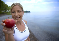 A healthy athlete holding a red apple on the beach; Shutterstock.com