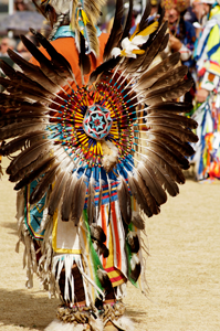 Photograph of a young person dressed in traditional Native American clothing, including beads and feathers.