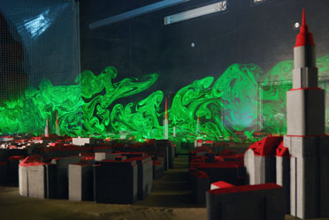 Image shows model of the city of Hamburg, Germany, with a cloud wafting over the roofs of the buildings. Green laser light makes the cloud visible.