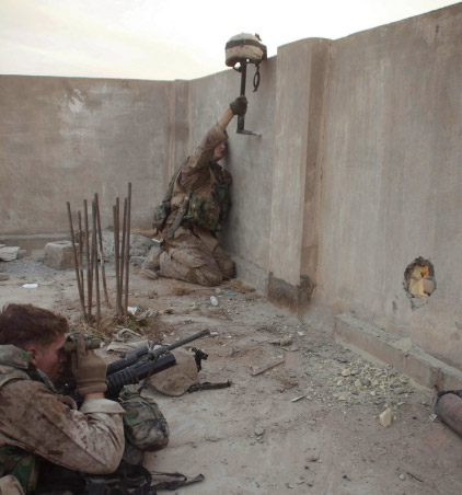A Marine uses a breaching tool to prop up his helmet up above a wall