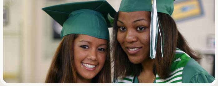 Close up of two high school students with green caps and gowns on graduation day