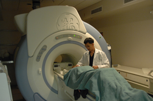 Photo of front of MRI machine with patient going into opening and technician assisting patient