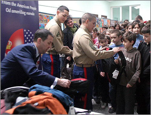 A Marine hands a backpack to a child