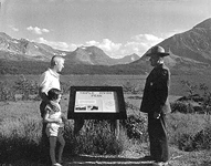 A roadside exhibit (with Ranger and visitors) describing Triple Divide Peak in Glacier N.P.