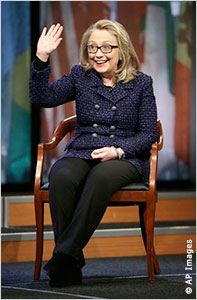 Hillary Rodham Clinton seated on stage, waving and smiling (AP Images)