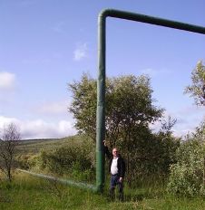 A man standing next to a pipeline that is elevated high above the ground to make way for giraffe migration