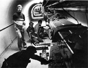 Merill Albertus (standing), Ken Meissner (foreground), Rine DeKing, and Gene Witt install a superconducting dipole magnet under a Main Ring magnet by gently sliding it into place