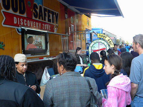 FSIS employees LCDR Sherry Spriggs and Dr. Jessica Forshee distribute food safety educational materials outside of the Food Safety Discovery Zone. The popular Food Safety Wheel Game is visible in the background.