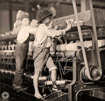 Young boys mending broken threads on a loom in a textile mill in Macon GA, circa 1909