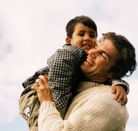 A father laughing as he holds is smiling son.