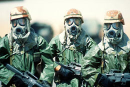 Dressed in rain suits, gloves and M-17A1 protective masks, three soldiers from the 82nd Airborne Division walk around their camp to acclimate their bodies to the heat of the Saudi summer during Operation Desert Shield. (by Staff F. Lee Corkran)