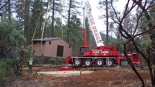 A bathroom building is set on a foundation using a crane at Hirz Bay Campground