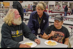 Sandy Hendrix, miembro de los Equipos de Relaciones con la Comunidad de FEMA conversa con sobrevivientes Tom Weinstein y Joey Perez en un albergue de la Cruz Roja Americana en la Escuela Superior Pleasantville.