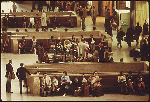 DOCUMERICA: Original Caption: Train passengers in the main hall of the 30th Street Station at Philadelphia, Pennsylvania. It is one of four or five stops made by Amtrak's Metroliners which made 16 round trips each day between New York City and Washington, District of Columbia. The corporation reported 18,000,000 passengers in the U.S. during 1974, an increase of 10 percent from the previous year. Despite more riders and revenue of $256.9 million, the management noted a deficit of $272.6 million, 04/1974 by Jim Pickerell.