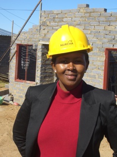 Woman wearing a NURCHA construction hat in front of the construction site