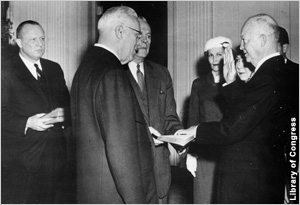 Dwight Eisenhower with one hand on book, other raised, as onlookers watch (Library of Congress)