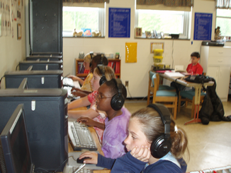 Row of computers with students with earphones intently working.