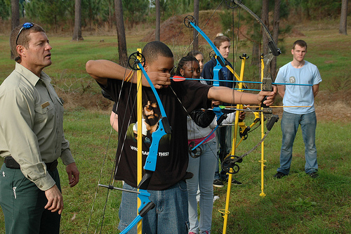 Natural Resource Manager Carl Petrick of the National Forests in Florida looks on as a high school student sets his sights on the archery range. Nearly 500 students from area schools attended the recent More Kids in the Woods event. (Photo Credit: Susan Blake, Public Affairs Specialist, National Forests of Florida)