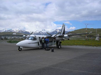 The image is of two people standing in front of a small, high-wing, twin-engine aircraft.