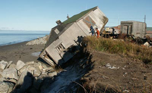 Photograph of seaside house that lies nearly on it's side with one end on higher sands and one side on the beach.