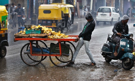 A fruit vendor struggles to cross a road with his cart in the rain in Bangalore, India.