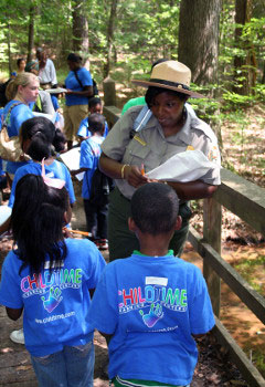 Image of female park ranger in woods speaking with group of children